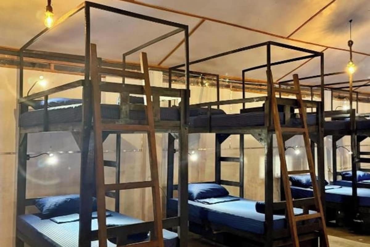 A dormitory-style room with bunk beds, wooden ladders, and hanging light fixtures.