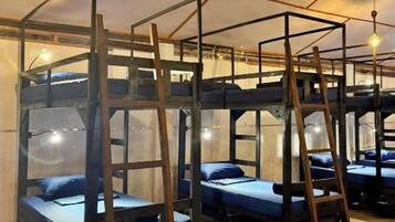 A dormitory-style room with bunk beds, wooden ladders, and hanging light fixtures.