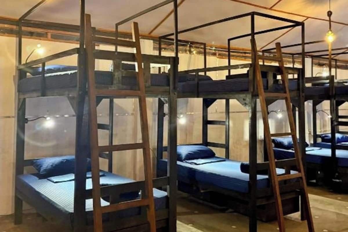 Habitación tipo dormitorio con literas, escaleras de madera e lámparas colgantes.