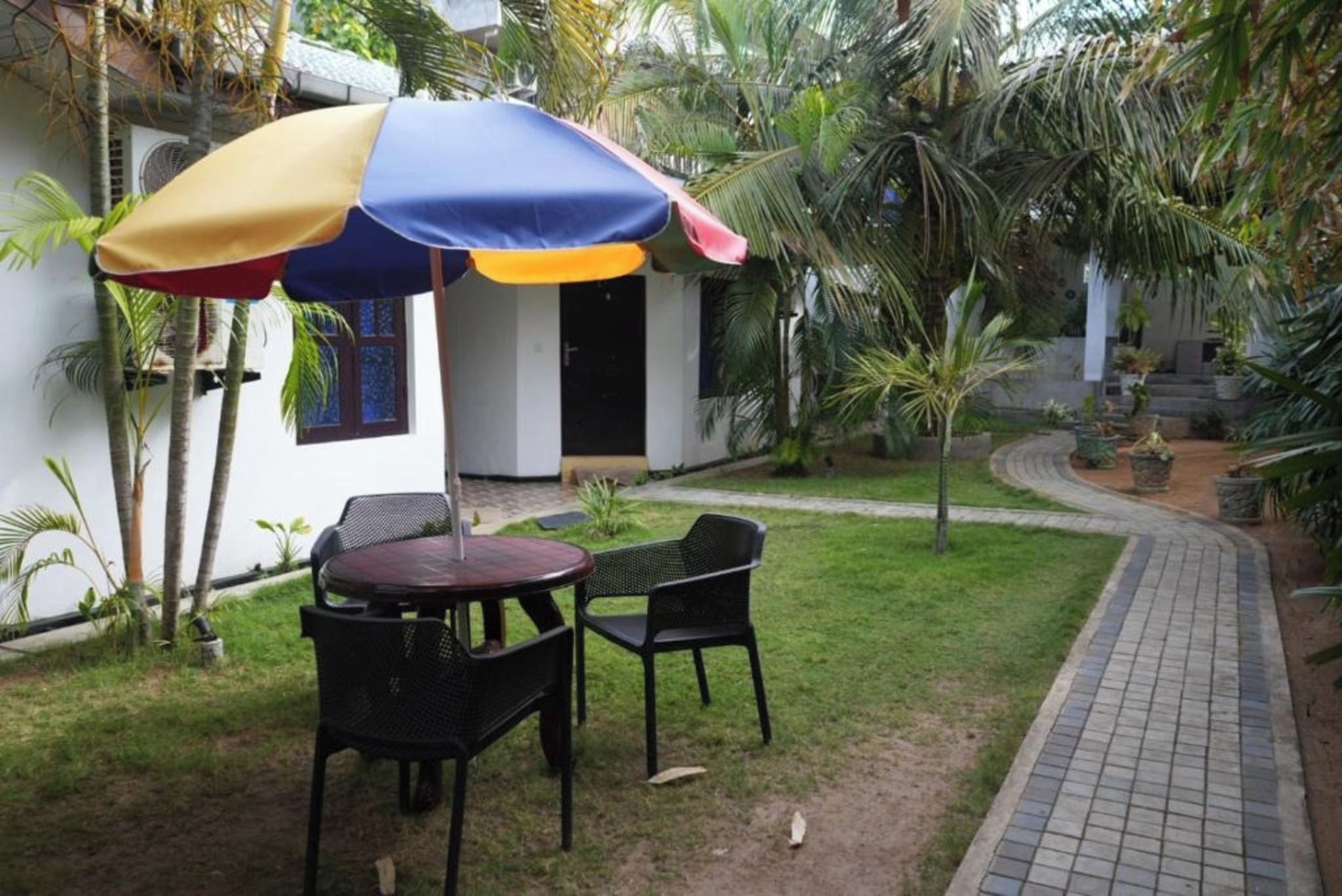 An outdoor seating area with a table and chairs, a colorful umbrella, and a pathway leading to a building.