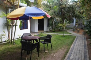 Zona d'estar a l'exterior amb taula i cadires, un para-sol colorit i un camí que condueix a un edifici.