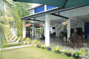 A covered outdoor area with seating, potted plants, and hanging plants. - The Calm Of8 Arugambay (Arugam Bay)