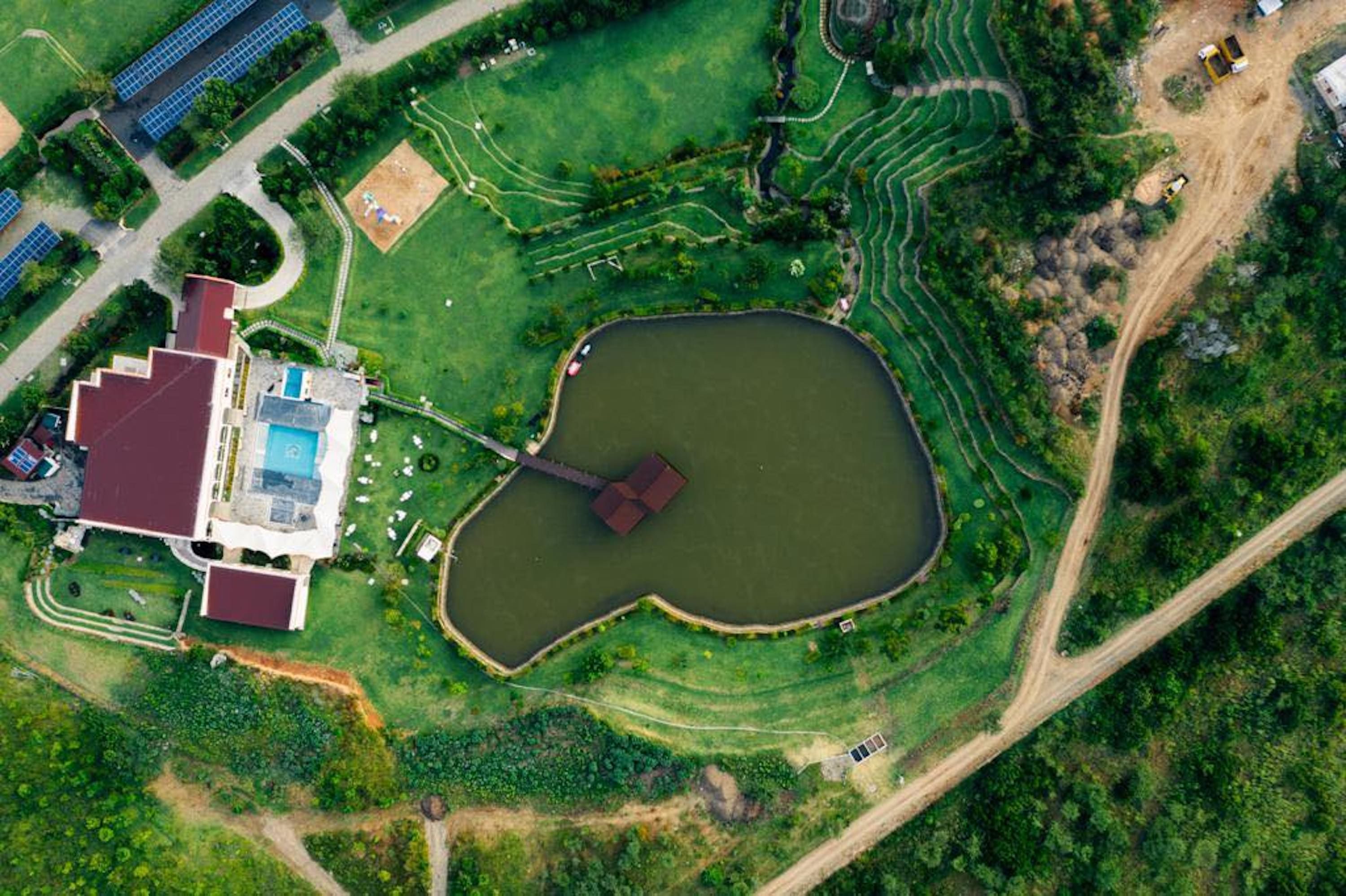 An aerial view of a property with a swimming pool, a heart-shaped pond, and terraced fields.