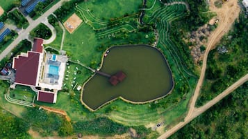 An aerial view of a property with a swimming pool, a heart-shaped pond, and terraced fields.