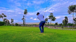 Una persona en un campo de golf bajo un cielo despejado y montañas a lo lejos.