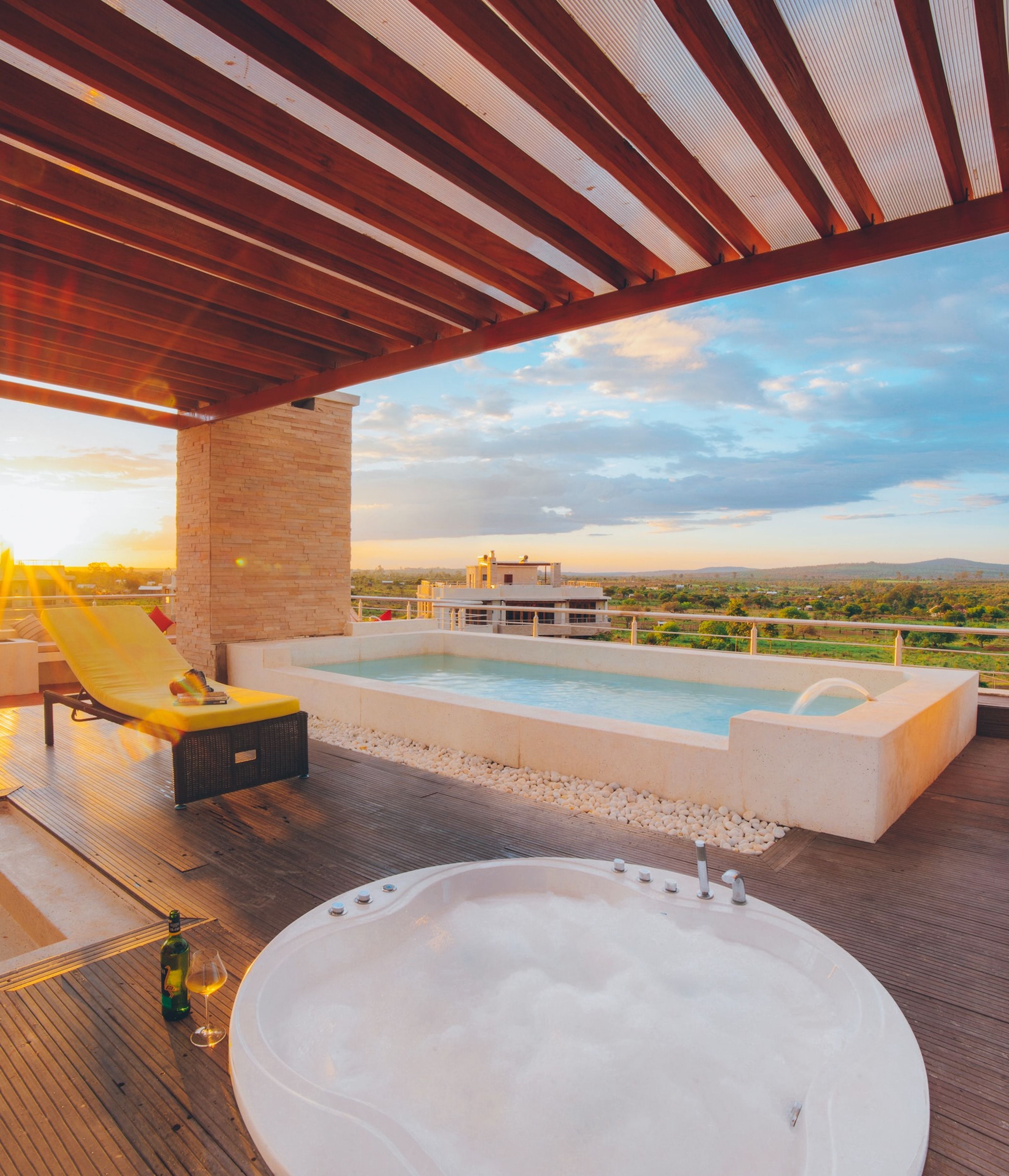 A rooftop pool area with a hot tub, lounge chairs, and a view of the landscape.
