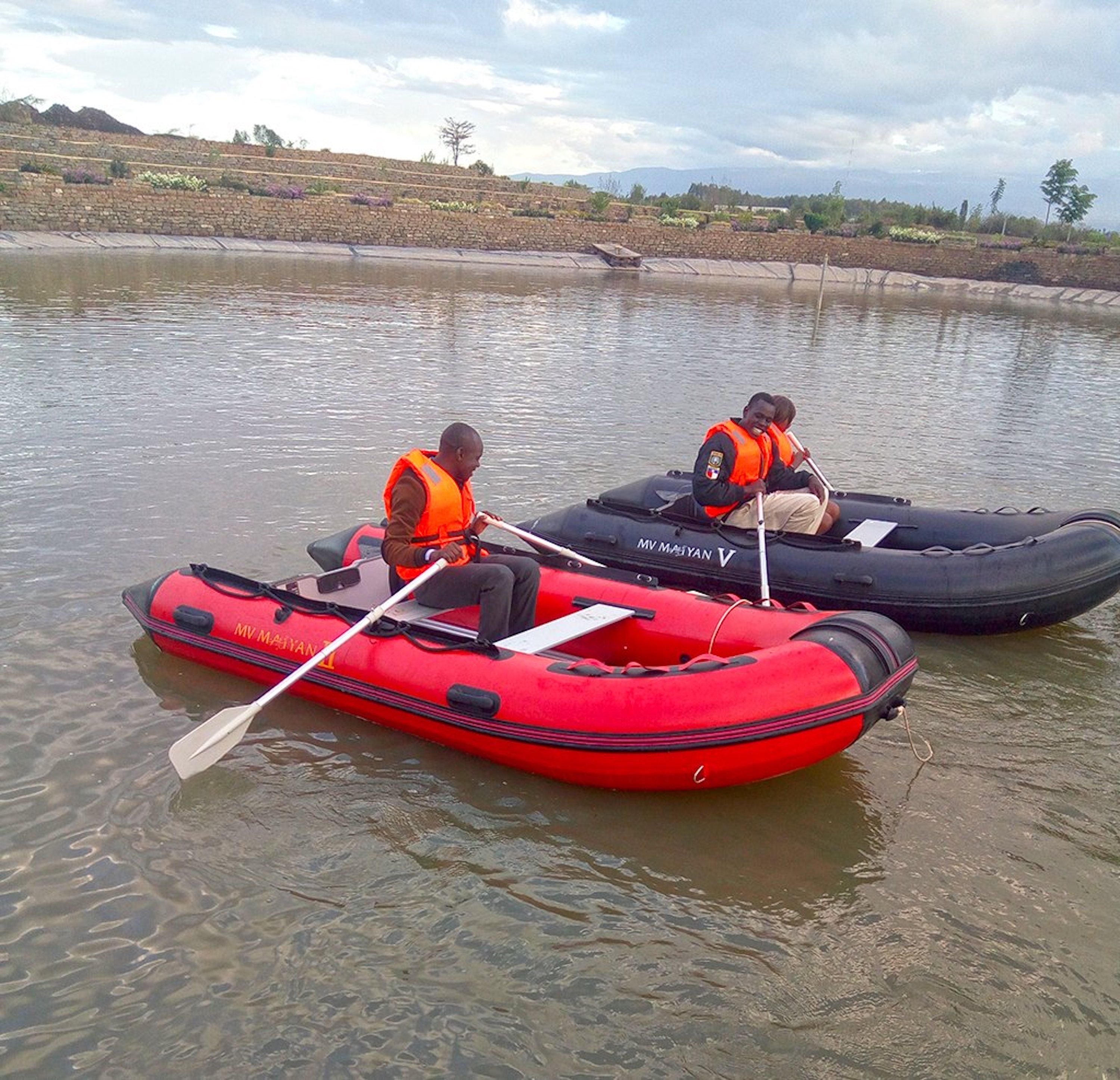 Two inflatable boats on a calm body of water with a stone embankment and vegetation in the background.