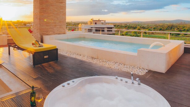 Un área de piscina en la azotea con un jacuzzi, sillones de descanso y vistas al paisaje.