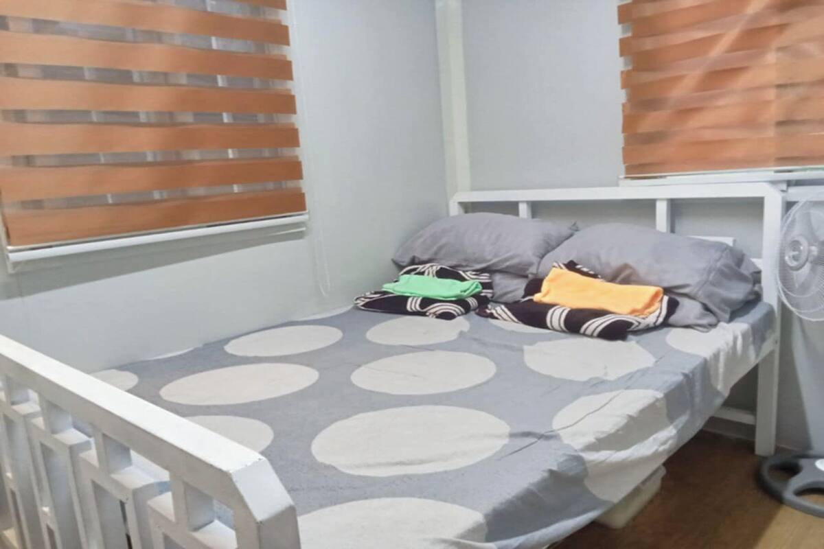 A single bed with a grey and white polka dot bedspread, a pillow, a blanket, and a toy car.