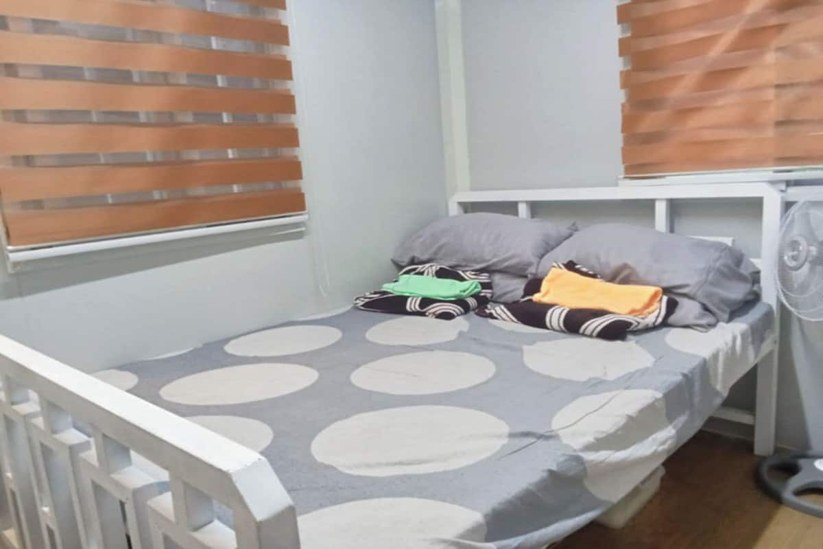 A single bed with a grey and white polka dot bedspread, a pillow, a blanket, and a toy car.
