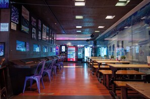 A restaurant interior with a long counter, purple chairs, wooden tables, vending machines, and a mural on the wall. - Kabul Party Hostel (Barcelona)