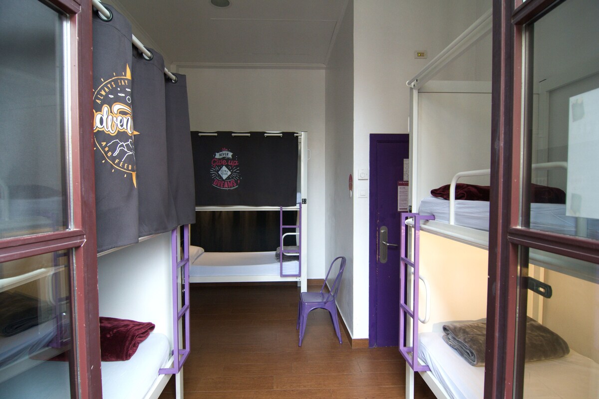 A dormitory room with bunk beds, a purple chair, and a blackboard with a logo.