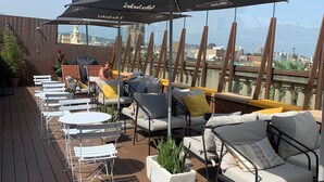 A rooftop terrace with outdoor seating, umbrellas, and a city view. - Kabul Party Hostel (Barcelona)