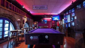 A billiards room with a pool table, tables, and chairs, and a sign indicating it's a billiards area. - Kabul Party Hostel (Barcelona)