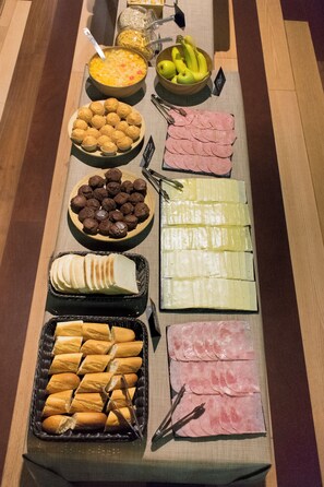 A buffet table with various food items including bread, pastries, and sliced meats. - Kabul Party Hostel (Barcelona)