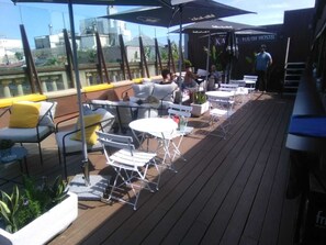 Un bar en la azotea con mesas y sillas al aire libre, resguardado por sombrillas.