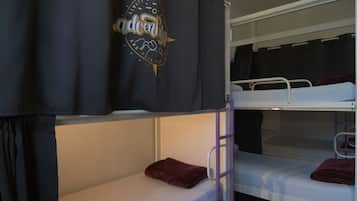 Quarto com beliches, cortina com um logotipo, cama com cobertor vermelho e colchão branco.