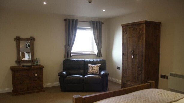 A bedroom with a bed, a wooden wardrobe, a leather chair, a dresser, and a window with curtains. - Woodman Inn (Bedale)