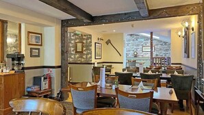 A restaurant with wooden tables and chairs, framed pictures on the walls, and a stone wall in the background. - Woodman Inn (Bedale)