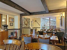 A restaurant with wooden tables and chairs, framed pictures on the walls, and a stone wall in the background.