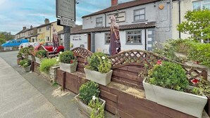 A pub with a signboard advertising food and fine ales, a car park to the rear, and a wooden fence with potted plants. - Woodman Inn (Bedale)