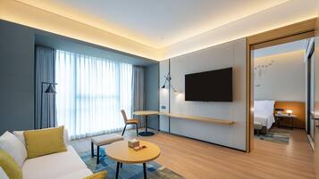 Una habitación de hotel moderna con sofá, una mesa redonda, televisión de pantalla plana, escritorio con lámpara y una cama.