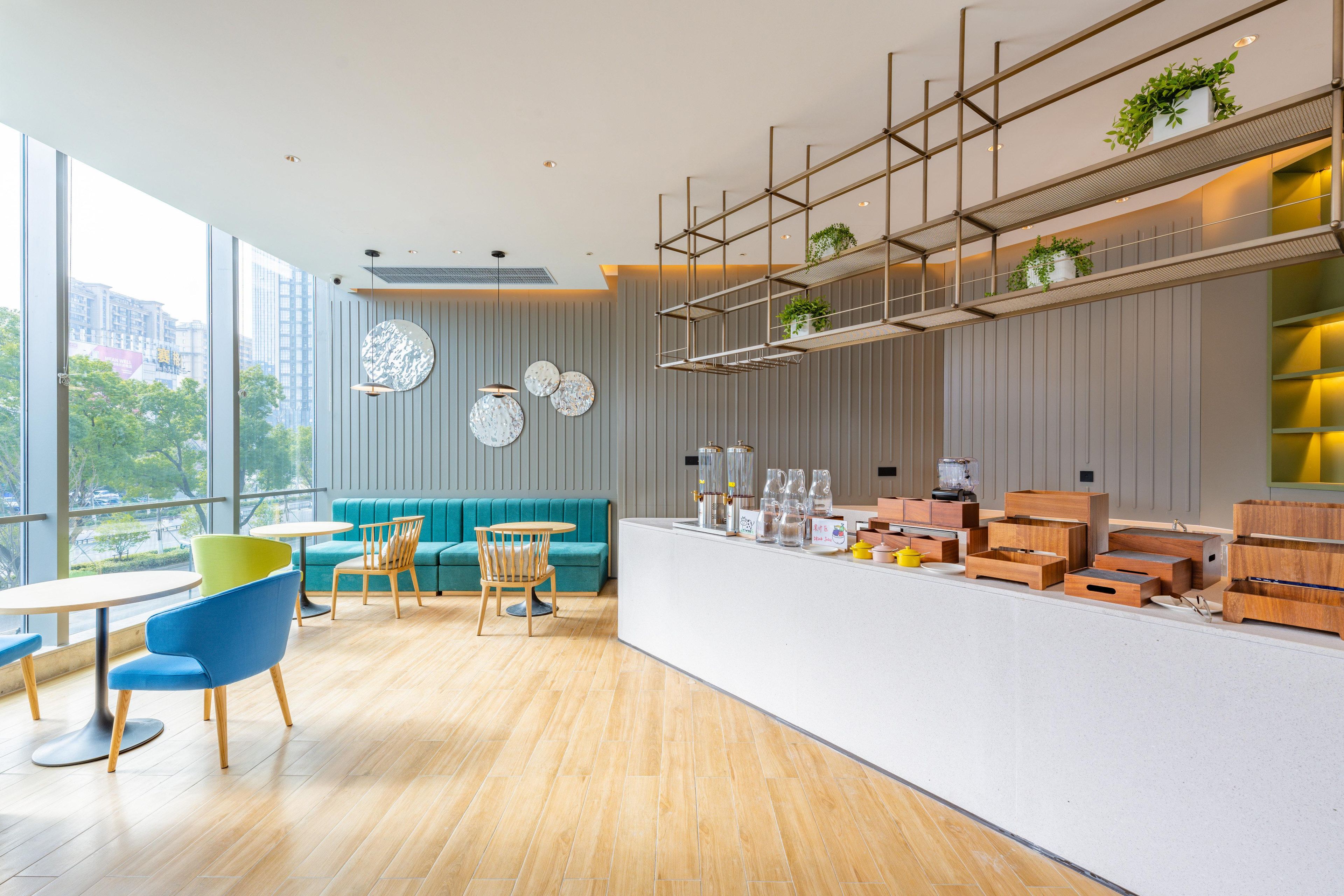 Un interior moderno con suelo de madera, un sofá azul verdoso, sillas azules y una encimera blanca con plantas y cajas de almacenaje.