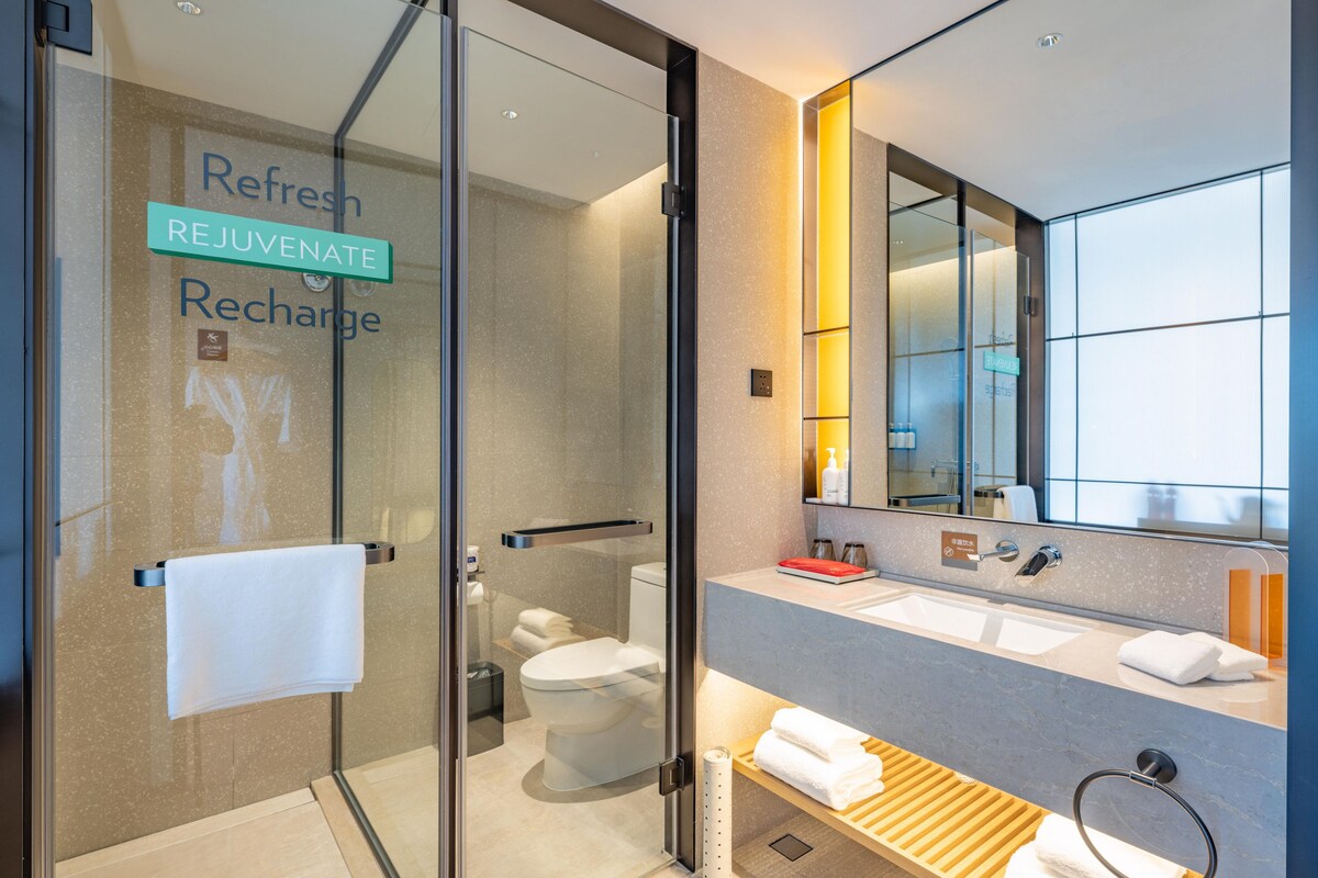A modern bathroom with a glass shower enclosure, a toilet, a sink with a mirror, and a towel rack.
