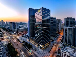 A modern hotel with a glass facade, surrounded by high-rise buildings and busy streets. - Even Suzhou Grand Canal (Suzhou)