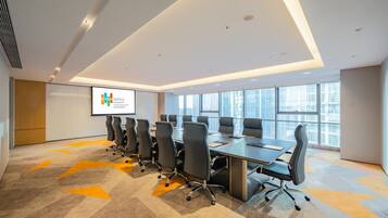 A conference room with a long table, multiple chairs, a projector screen, and large windows.