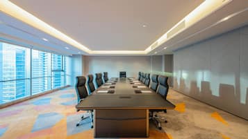 Un salón de conferencias con una larga mesa, sillas y vistas a edificios a través de amplios ventanales.