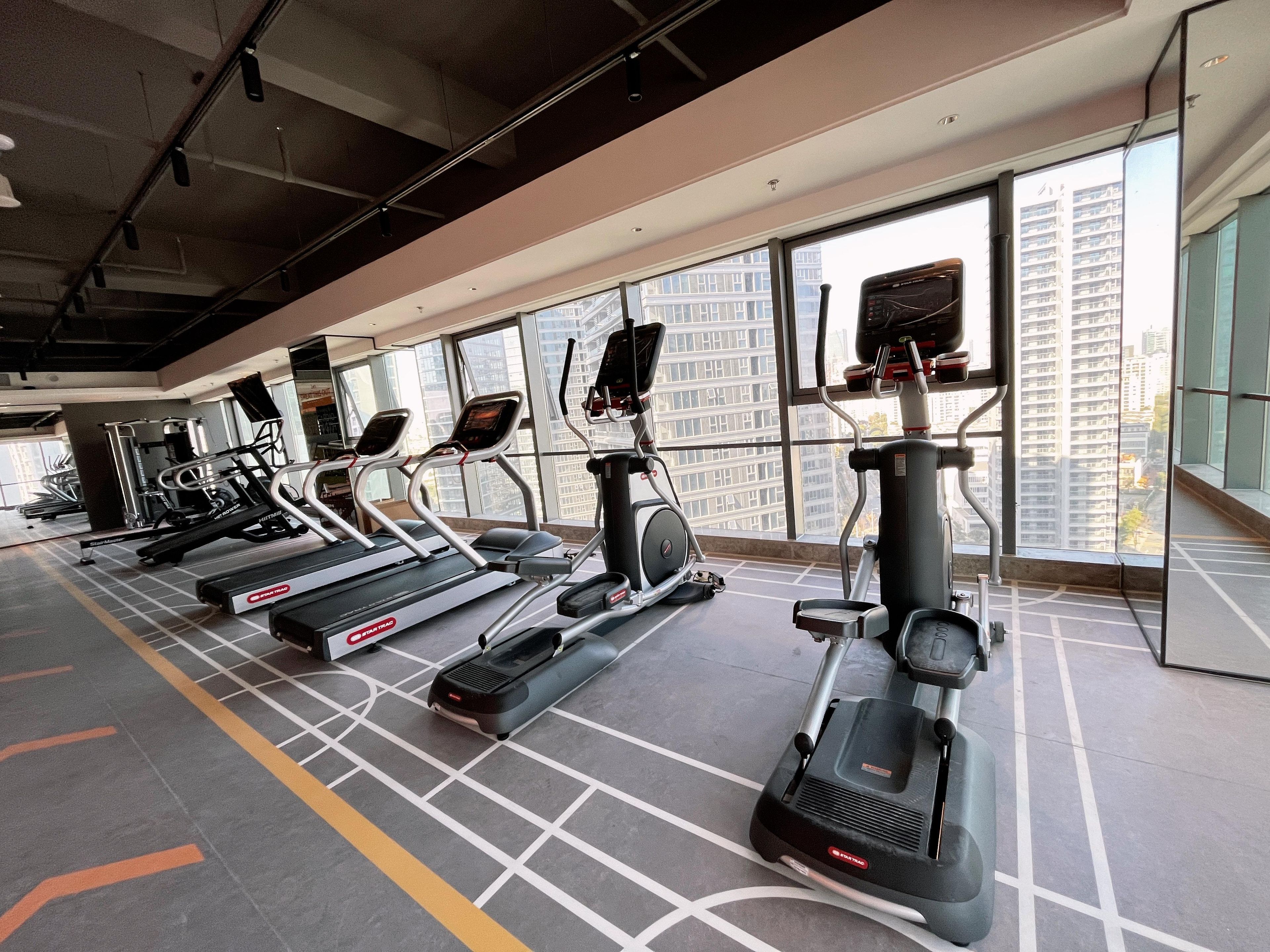 Un gimnasio con cintas de correr, elípticas y un espejo grande.