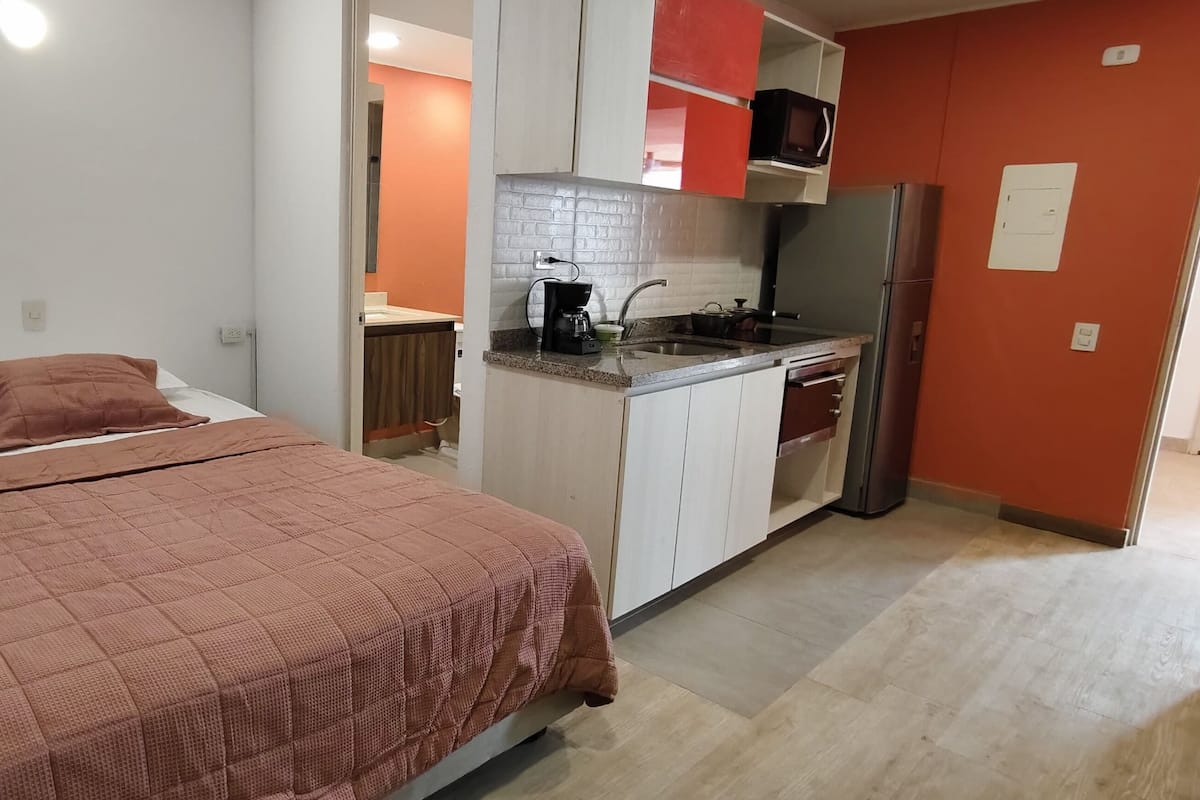 A bedroom with a bed and a kitchenette.