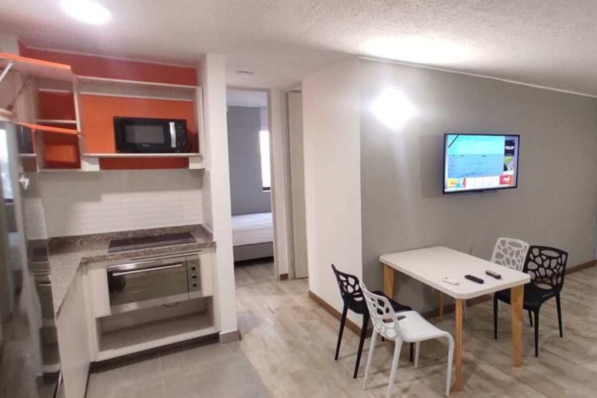 Una sala moderna con una mesa de comedor, sillas, un televisor y un amplio ventanal.