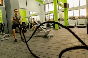 Un gimnasio con equipo de ejercicio, una caminadora y una persona usando una cuerda de batalla.