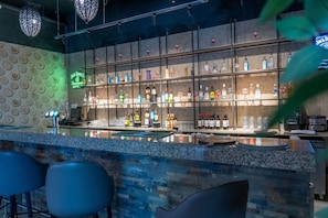 Un espace bar doté d’un comptoir, de tabourets et d’une variété de bouteilles et de verres.