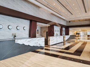 A hotel reception area with marble counters, clocks indicating different cities, and a modern design. - Vogo Grand Hotel (Dubai)