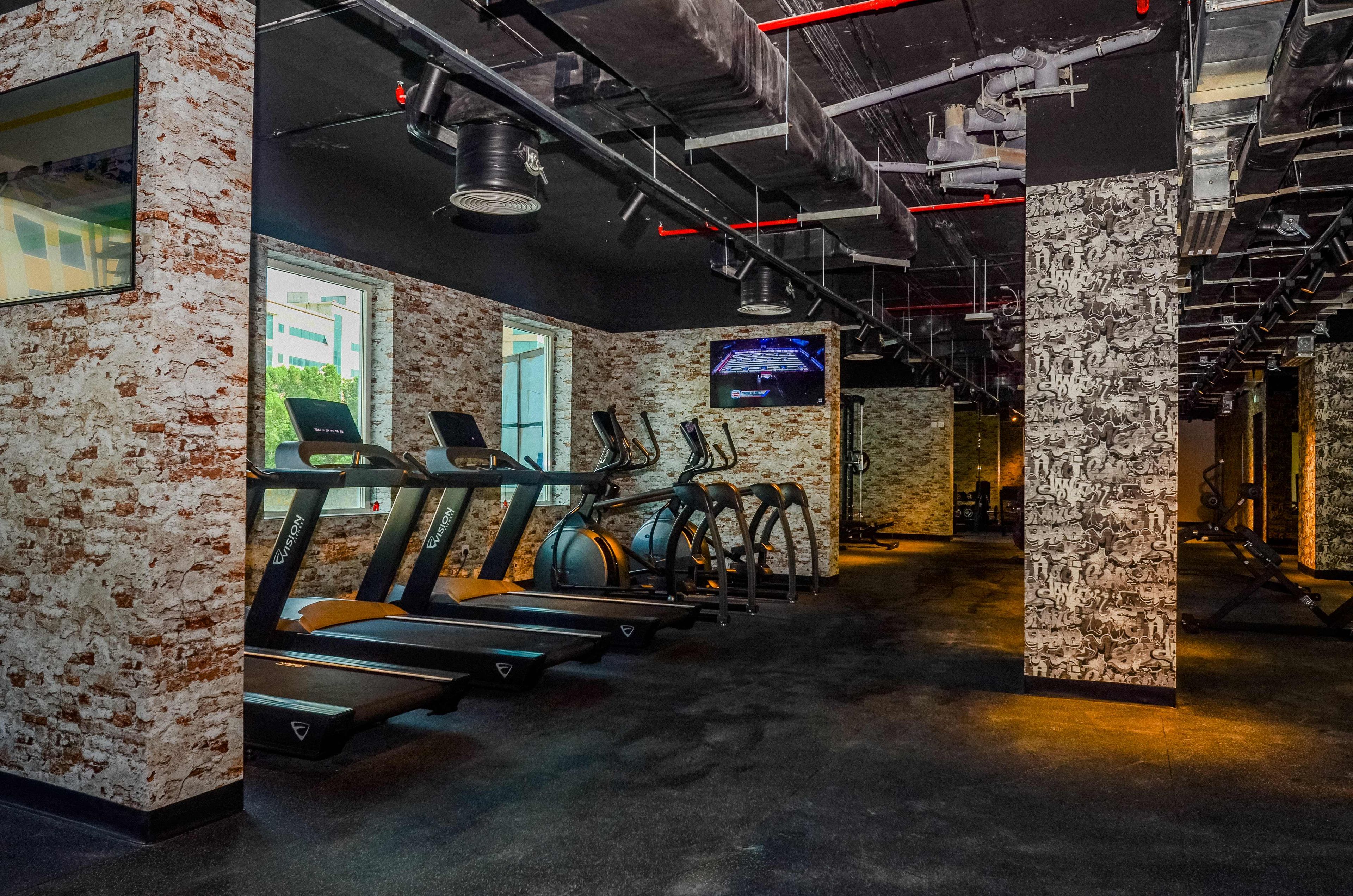 A gym with treadmills, stationary bikes, and a television screen.