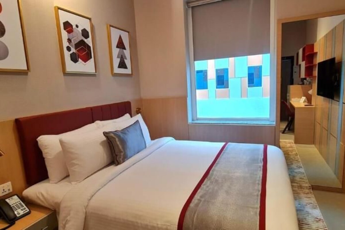 A hotel room with a bed, a desk with a telephone, artwork on the wall, a television, and a window with a view.