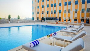 A swimming pool with lounge chairs and a building with a geometric facade. - Vogo Grand Hotel (Dubai)