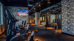 A gym with exercise equipment, a TV screen, and a graffiti wall. - Vogo Grand Hotel (Dubai)