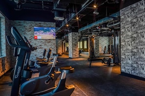 Un gimnasio con equipo de ejercicio, una pantalla de televisión y un muro con grafitis.