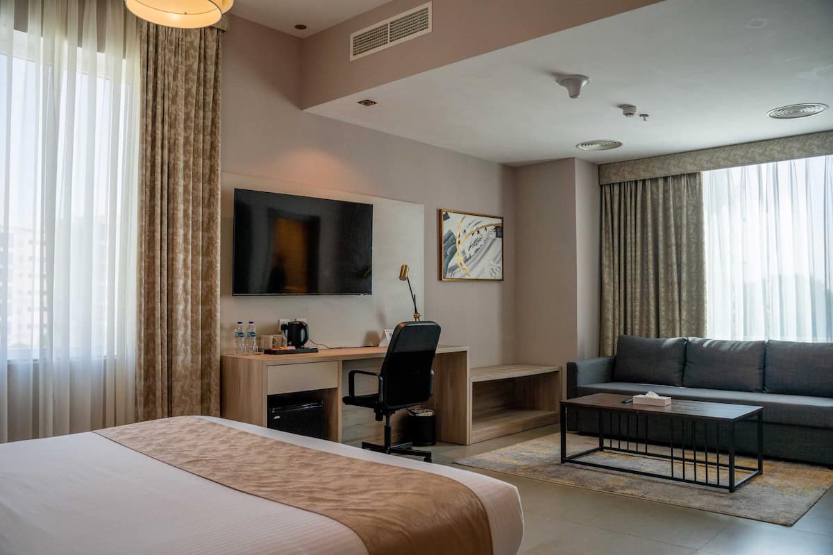 Una habitación de hotel con cama, escritorio, silla, sofá, televisor y obras de arte.