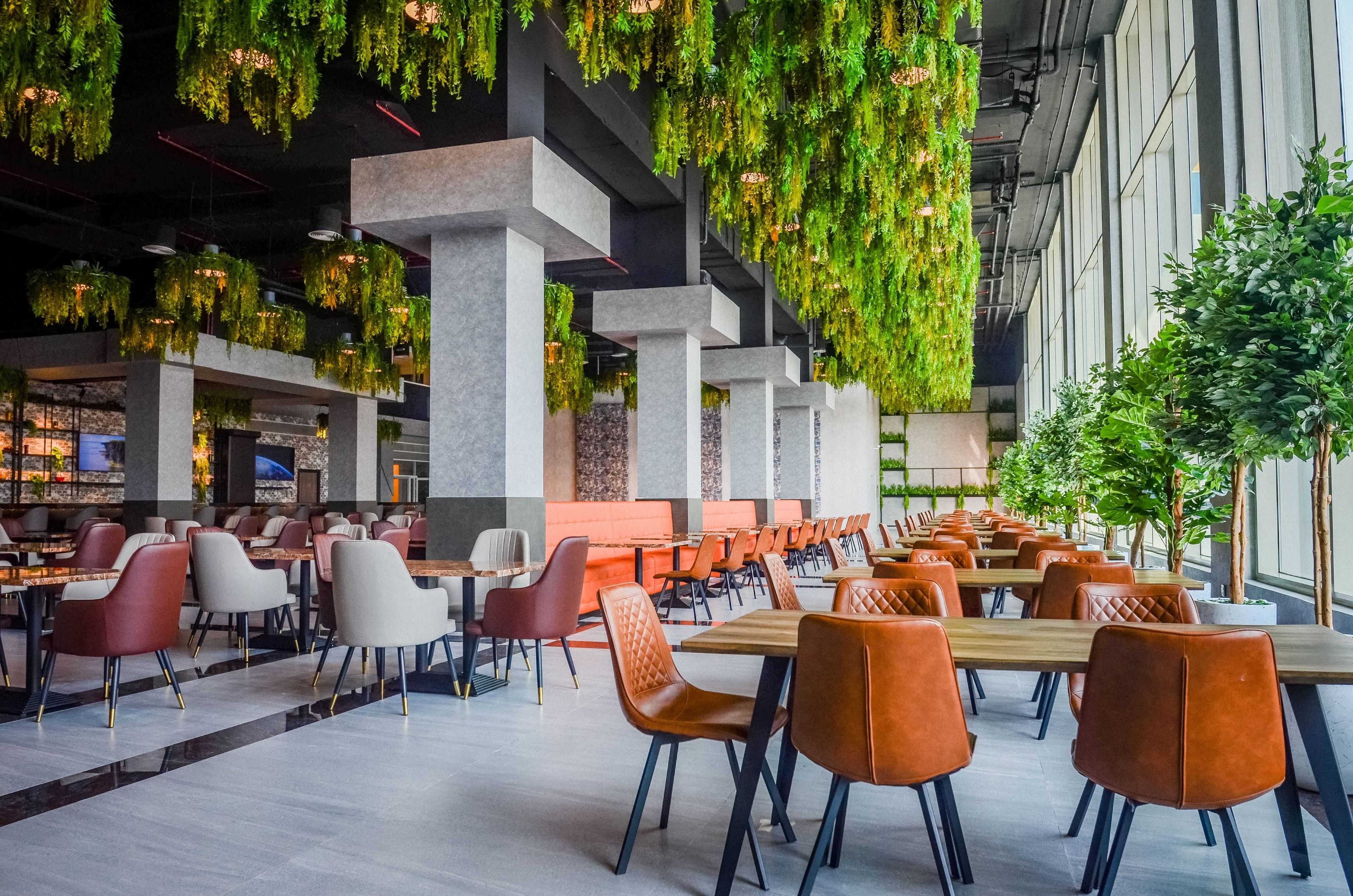 A modern dining area with tables and chairs, hanging greenery, and a view of the outdoors.