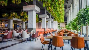 A modern dining area with tables and chairs, hanging greenery, and a view of the outdoors.