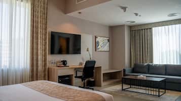 A hotel room with a bed, desk, chair, sofa, TV, and artwork.
