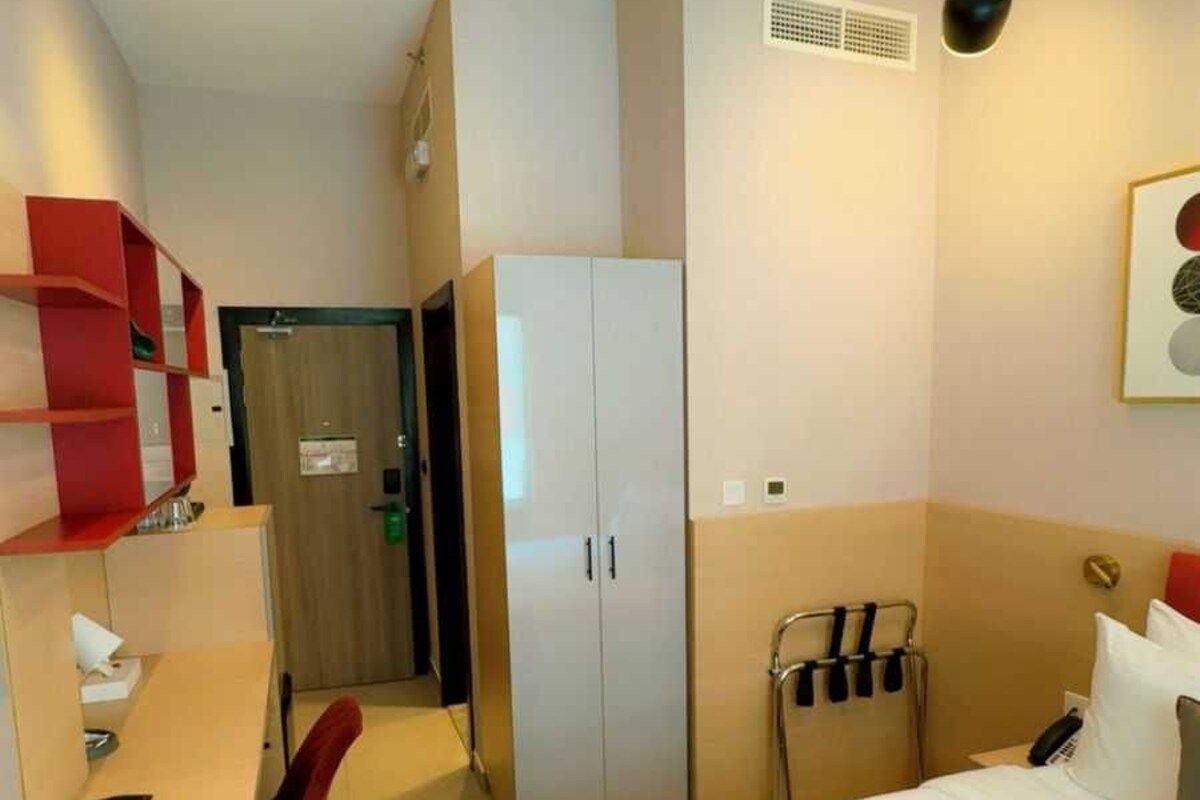 A hotel room with a bed, a desk, a chair, a wardrobe, and a hanging light fixture.