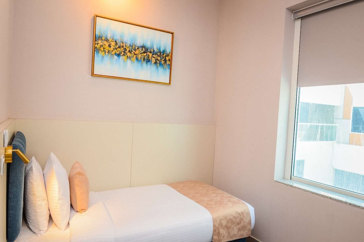 Ein Hotelzimmer mit Bett, Kissen, einem Gemälde und einem Fenster.