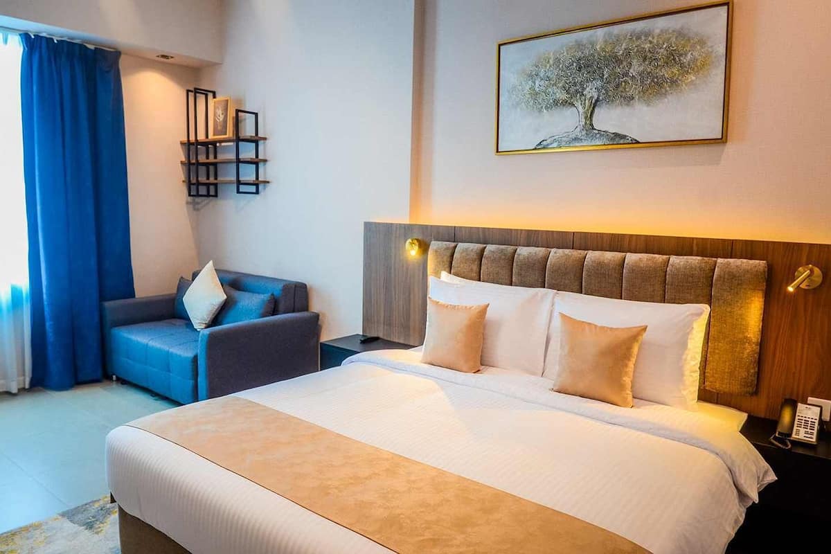 Una habitación de hotel con una cama, un sofá, un estante con fotografías y un cuadro de un árbol.