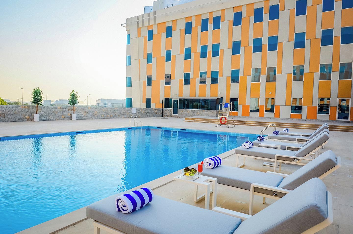 Piscina com espreguiçadeiras e um edifício com fachada geométrica.